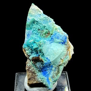 May include: A vibrant mineral specimen featuring a mix of blue, turquoise, and brown hues. The rough, textured surface displays crystalline formations and a unique, natural aesthetic. The mineral is mounted on a small, dark base.