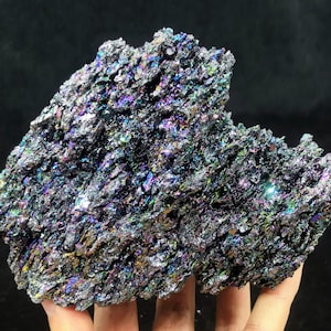 Peut inclure: Un gros cristal de carbure de silicium brut, iridescent, gris foncé, rugueux et irrégulier. Le cristal a un éclat métallique et présente un arc-en-ciel de couleurs.