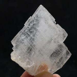 Può includere: Un cristallo trasparente bianco translucido con una struttura a strati sovrapposti. Il cristallo ha una forma geometrica ed è un esemplare minerale naturale.
