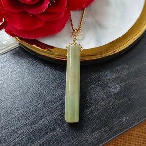 Könnte beinhalten: Eine goldene Kettenkette mit einem hellgrünen Jade-Anhänger in Form eines langen, dünnen Rechtecks.