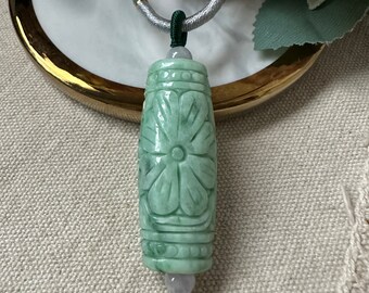May include: A green jade pendant necklace with a carved flower design. The pendant is attached to a green and silver cord.