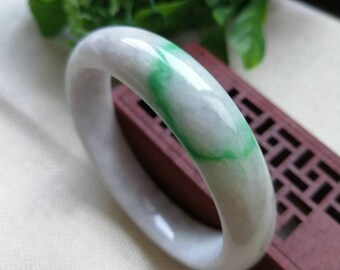 May include: A white jade bangle with a green swirl design. The bangle is smooth and polished.