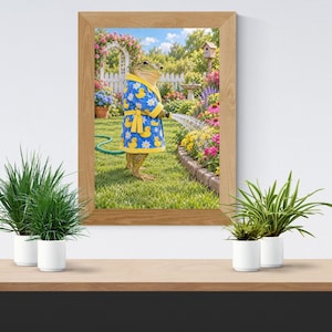 Op de afbeelding: Een ingelijste kunstdruk van een kikker in een blauwe badjas met een patroon van gele badeendjes en witte madeliefjes. De kikker staat in een tuin en houdt een groene tuinslang vast om water te sproeien over een bed met kleurrijke bloemen.