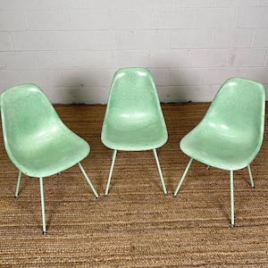 May include: Three light green fiberglass chairs with metal legs. The chairs are arranged in a row on a brown woven rug.