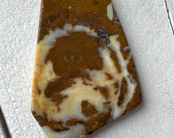 May include: A brown and white agate stone with a swirling pattern. The stone is irregularly shaped and has a smooth, polished surface.