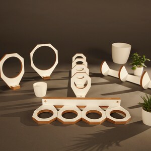 May include: White wooden wall mounted plant hangers in various shapes and sizes. Some hangers are round, some are octagonal, and some are shaped like a teardrop. The hangers are all made of white wood with a natural wood finish on the edges.