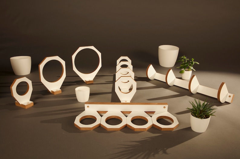 May include: White wooden wall mounted plant hangers in various shapes and sizes. Some hangers are round, some are octagonal, and some are shaped like a teardrop. The hangers are all made of white wood with a natural wood finish on the edges.