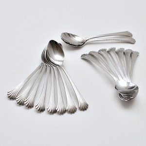 May include: A set of 14 silver teaspoons with a decorative, fluted design. The spoons are arranged in a fan shape, with the handles pointing outwards.