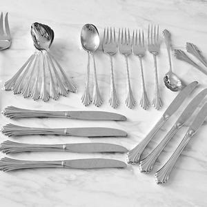 May include: A set of silver flatware, including forks, knives, and spoons. The flatware is arranged on a white marble surface.