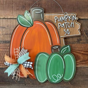 May include: Wooden pumpkin-shaped sign with an orange pumpkin and two green pumpkins. The sign reads "Pumpkin Patch 5¢" and is decorated with a bow. The sign is designed for fall and autumn decor.