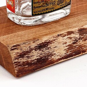 May include: A wooden coaster with a natural, rustic finish. The coaster has a live edge and a light brown color with darker brown streaks. The coaster is perfect for displaying a bottle of liquor.
