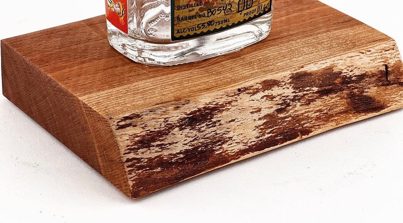 May include: A wooden coaster with a natural, rustic finish. The coaster has a live edge and a light brown color with darker brown streaks. The coaster is perfect for displaying a bottle of liquor.