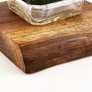 May include: A close-up of a wooden coaster with a clear glass bottle on top. The coaster is made of dark wood with a natural grain pattern.