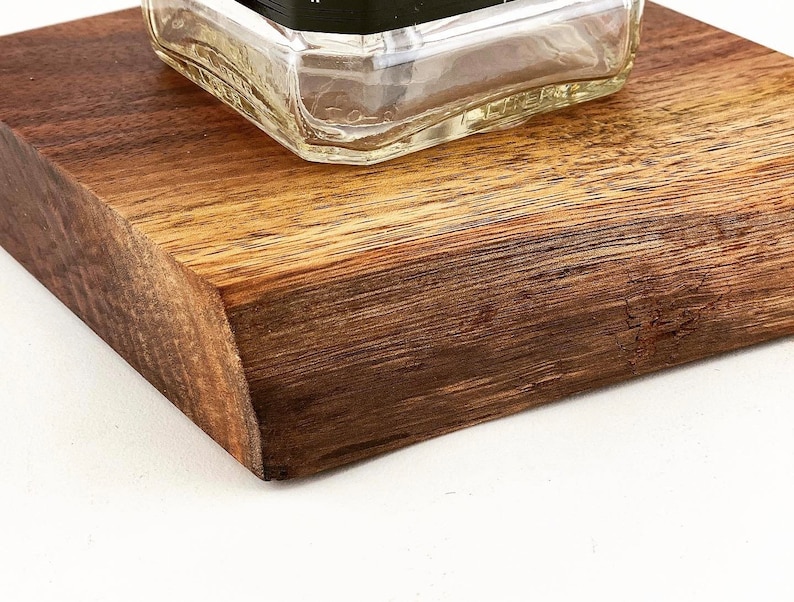 May include: A close-up of a wooden coaster with a clear glass bottle on top. The coaster is made of dark wood with a natural grain pattern.
