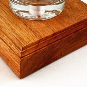 May include: Close-up of a wooden base with a beveled edge. The base is made of cherry wood and has a rich reddish-brown color. The wood grain is visible and adds to the natural beauty of the base.