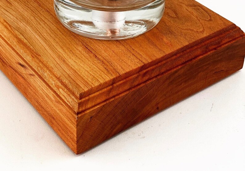 May include: Close-up of a wooden base with a beveled edge. The base is made of cherry wood and has a rich reddish-brown color. The wood grain is visible and adds to the natural beauty of the base.