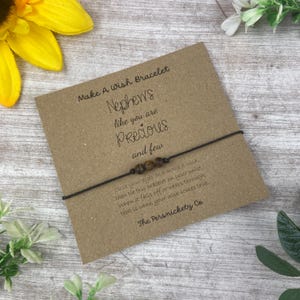 May include: A brown card with the text "Make A Wish Bracelet" and "Nephew's like you are Precious and few". A brown string bracelet with brown beads is tied around the card.