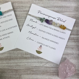 May include: A silver bracelet with various colored gemstones, including amethyst, fluorite, moonstone, and citrine. The bracelet is displayed on a white card with the text "Perimenopause Relief" and descriptions of the gemstones' benefits.
