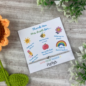 Könnte beinhalten: Ein silbernes Perlenarmband mit einem Sternanhänger wird auf einer weißen Karte mit bunten Illustrationen und dem Text "Thank You Mrs Scott for..." und "LOVE FROM HARRIS" präsentiert. Eine gehäkelte Sonnenblume befindet sich im Hintergrund.