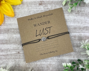 May include: A black string bracelet with a silver charm that says "Wander Lust". The bracelet is on a brown card with the text "Make A Wish Bracelet" and "The Persnickety Co."