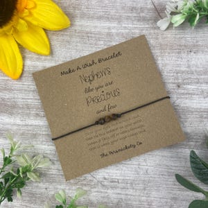 May include: A brown wish bracelet with brown beads and a card that reads "Make A Wish Bracelet Nephews like you are Precious and few close your eyes and make a wish then tie this bracelet on your wrist. When it falls off or wears through. that is when your wish comes true. The Persnickety Co"