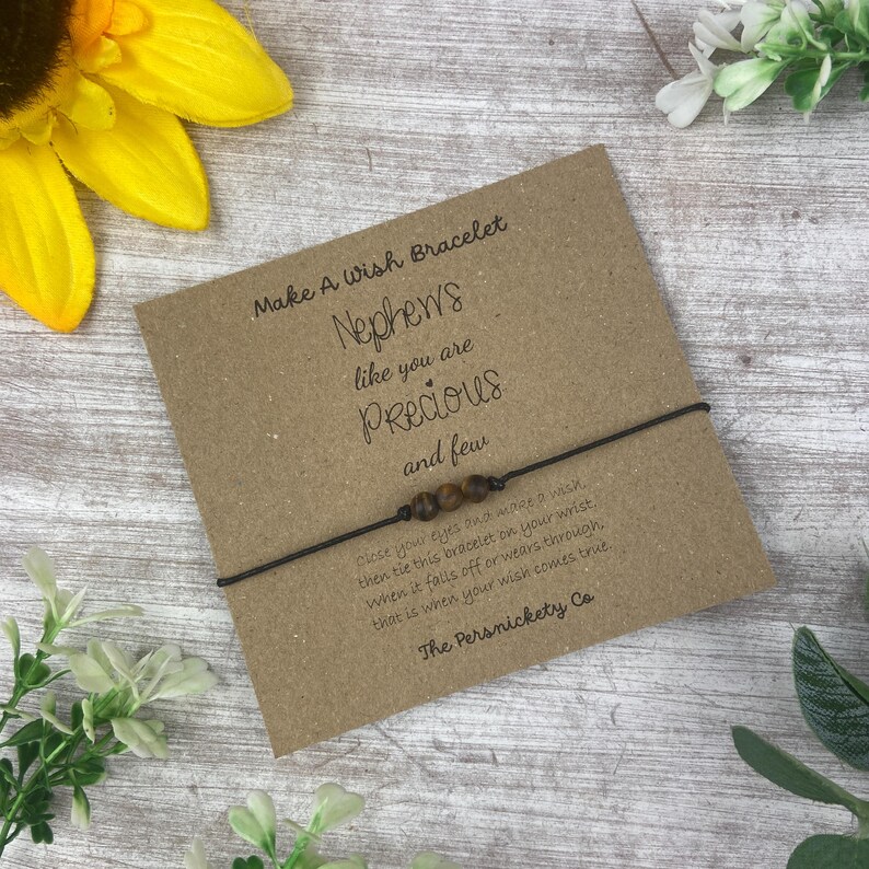 May include: A brown wish bracelet with brown beads and a card that reads "Make A Wish Bracelet Nephews like you are Precious and few close your eyes and make a wish then tie this bracelet on your wrist. When it falls off or wears through. that is when your wish comes true. The Persnickety Co"