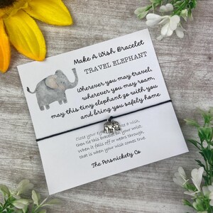 May include: A white card with black text that reads "Make A Wish Bracelet Travel Elephant" and "Wherever you may travel, wherever you may roam, may this tiny elephant go with you and bring you safely home".  The card has a small gray elephant illustration and a silver charm of an elephant attached to a black string.