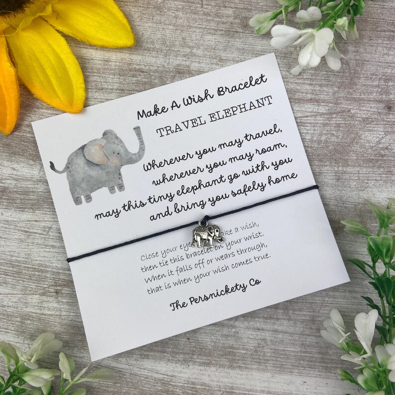 May include: A white card with black text that reads "Make A Wish Bracelet Travel Elephant" and "Wherever you may travel, wherever you may roam, may this tiny elephant go with you and bring you safely home".  The card has a small gray elephant illustration and a silver charm of an elephant attached to a black string.