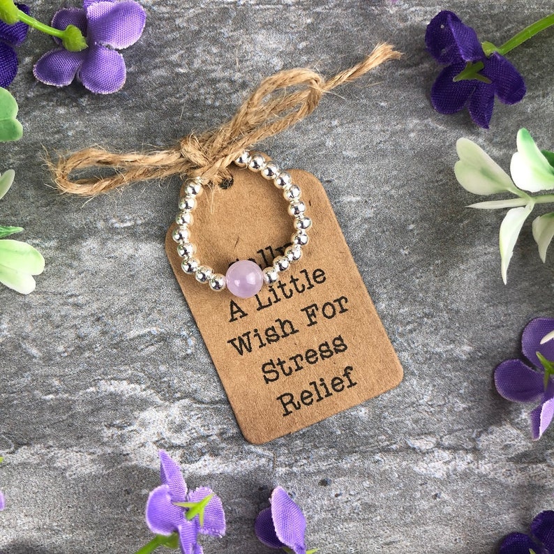 May include: A silver beaded ring with a light purple stone. The ring is tied with a brown twine bow and a brown tag that reads "A Little Wish For Stress Relief".