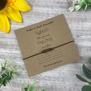 May include: A brown string bracelet with wooden beads and a card that reads "Make A Wish Bracelet Nephews like you are Precious and few" and "Place your eyes and make a wish then tie this bracelet on your wrist. When it falls off or wears through, this is when your wish comes true. The Persnickety Co."