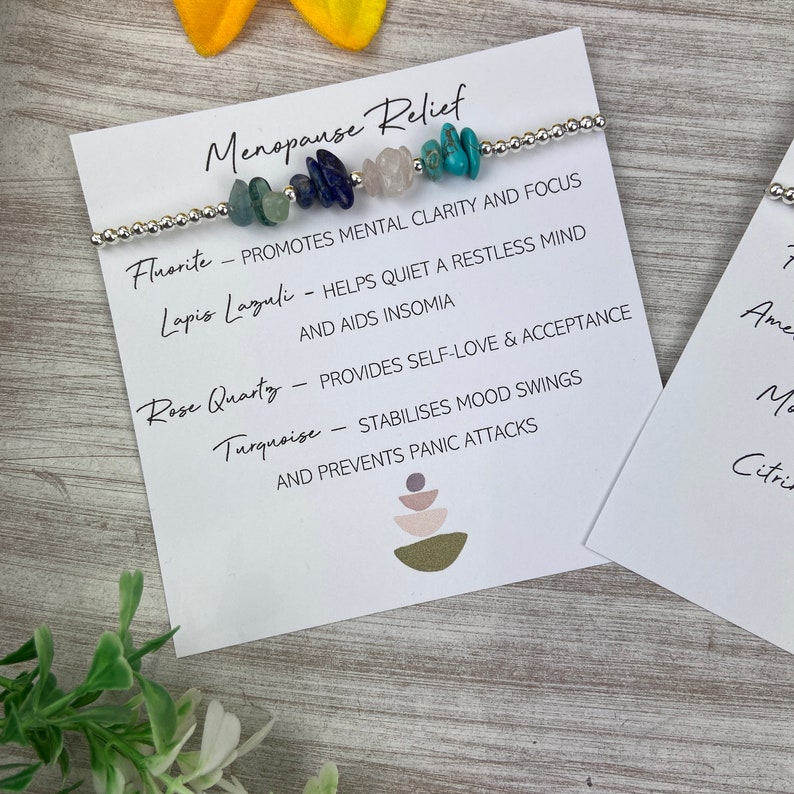 May include: A bracelet with various colored stones, including turquoise, rose quartz, lapis lazuli, and fluorite. The bracelet is accompanied by a card that lists the stones and their associated benefits for menopause relief.