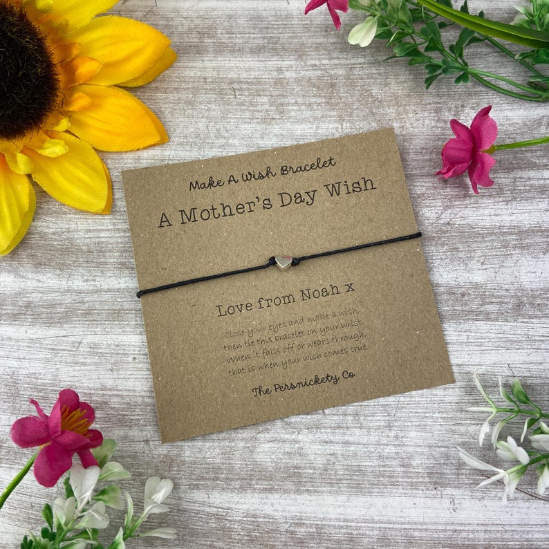 May include: A brown card with the text "Make A Wish Bracelet A Mother's Day Wish" and "Love from Noah x" with a black string bracelet with a silver heart charm. The card also includes instructions on how to make a wish with the bracelet.