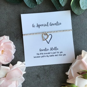May include: A white card with the text "A Special Auntie" and "Auntie Stella" with a silver bracelet with a double heart charm. The card reads "This little bracelet is just for you because you're my Auntie and I love you."