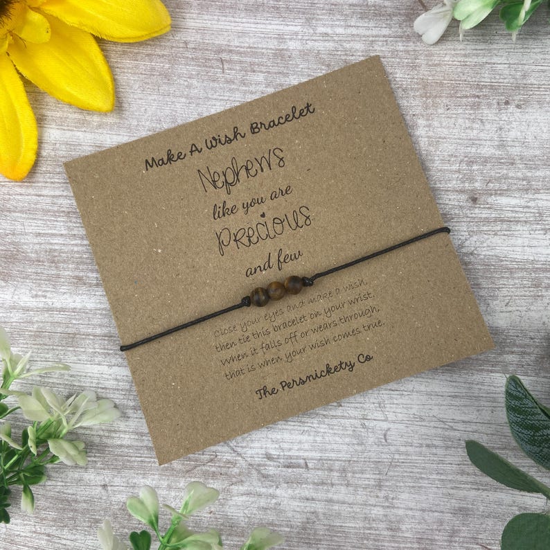 May include: A brown string bracelet with brown beads and a card that reads "Make A Wish Bracelet Nephews like you are Precious and few Close your eyes and make a wish, then tie this bracelet on your wrist, when it falls off or wears through, that is when your wish comes true. The Persnickety Co."