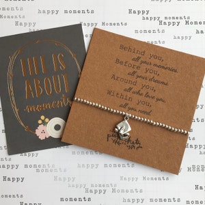May include: A silver charm bracelet with a small charm that says "tickety" on it. The bracelet is on a card with the text "Life is about moments" and "Behind you, all your memories. Before you, all your dreams. Around you, all who love you. Within you, all you need."