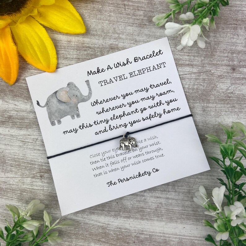 May include: A black string bracelet with a silver elephant charm. The card attached to the bracelet reads "Make A Wish Bracelet Travel Elephant" and includes a message about making a wish and tying the bracelet on your wrist. The charm will fall off when your wish comes true. The card is signed "The Persnickety Co."