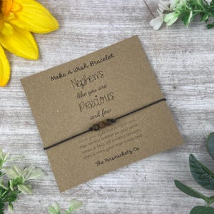May include: A brown string bracelet with brown beads and a card that reads "Make A Wish Bracelet Nephews like you are Precious and few close your eyes and make a wish then tie this bracelet on your wrist when it falls off or wears through that is when your wish comes true The Persnickety Co"