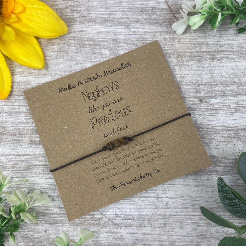 May include: A brown string bracelet with brown beads and a card that reads "Make A Wish Bracelet Nephews like you are Precious and few close your eyes and make a wish then tie this bracelet on your wrist when it falls off or wears through that is when your wish comes true The Persnickety Co"