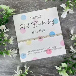 Op de afbeelding: Een witte kaart met kleurrijke stippen en de tekst "Happy 21st Birthday Jessica" en een zilveren armband met een sterbedel. De kaart zegt "This little bracelet is just to say have a very special & happy 21st birthday!"