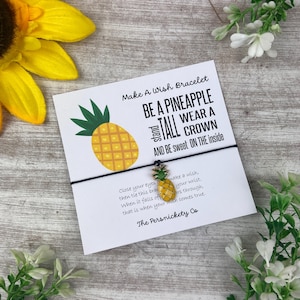 Puede incluir: Un brazalete de cuerda negro con un dije de piña. La tarjeta adjunta al brazalete dice "Make A Wish Bracelet, Be A Pineapple Stand Tall Wear A Crown And Be Sweet On The Inside". La tarjeta también incluye instrucciones sobre cómo hacer un deseo con el brazalete.