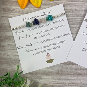 May include: A bracelet with various colored stones, including turquoise, rose quartz, lapis lazuli, and fluorite. The bracelet is accompanied by a card that lists the stones and their associated benefits for menopause relief.