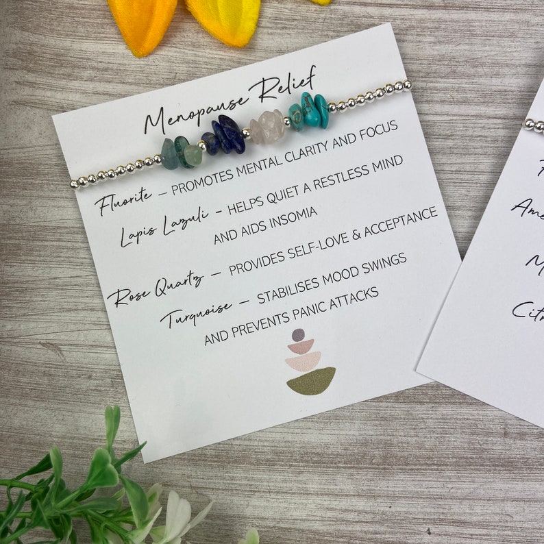 May include: A bracelet with various colored stones, including turquoise, rose quartz, lapis lazuli, and fluorite. The bracelet is accompanied by a card that lists the stones and their associated benefits for menopause relief.
