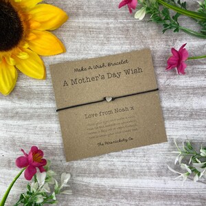 May include: A brown card with the text "Make A Wish Bracelet A Mother's Day Wish" and "Love from Noah x" with a black string bracelet with a silver heart charm.