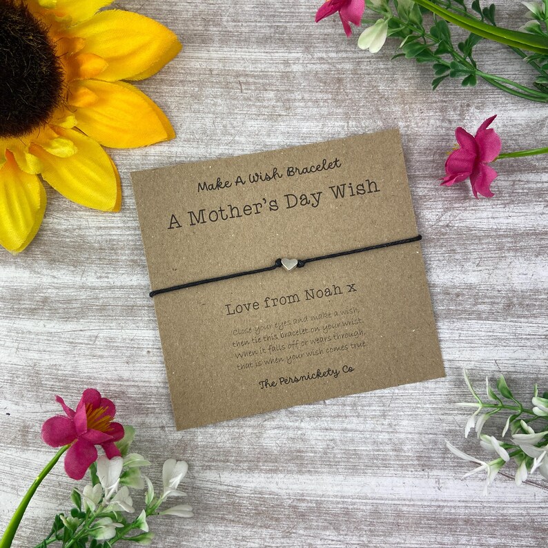 May include: A brown card with the text "Make A Wish Bracelet A Mother's Day Wish" and "Love from Noah x" with a black string bracelet with a silver heart charm.