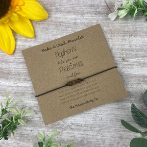 May include: A brown string bracelet with brown beads and a card that reads "Make A Wish Bracelet Nephews like you are Precious and few close your eyes and make a wish then tie this bracelet on your wrist when it falls off or wears through that is when your wish comes true. The Persnickety Co."