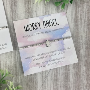 May include: A silver bracelet with a small angel charm. The bracelet is on a white card with the text "Worry Angel" and a message about using the bracelet to help calm worries.