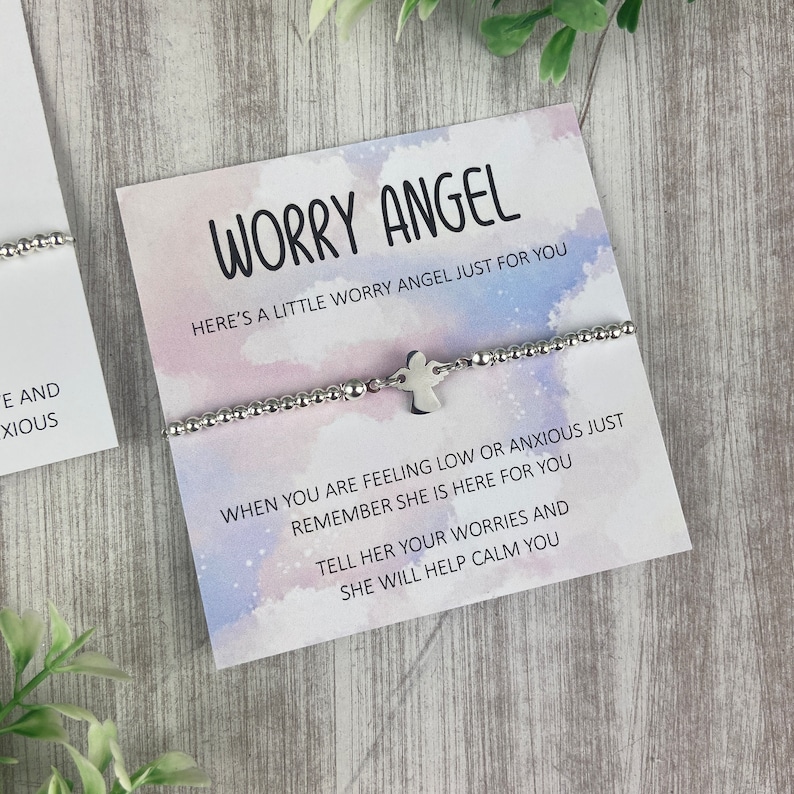 May include: A silver bracelet with a small angel charm. The bracelet is on a white card with the text "Worry Angel" and a message about using the bracelet to help calm worries.