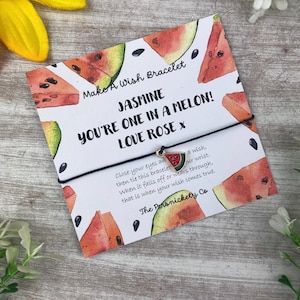Op de afbeelding: Een zwart koordarmband met een watermeloenbedel. De kaart luidt "Make A Wish Bracelet Jasmine You're One In A Melon! Love Rose X" en bevat instructies voor het maken van een wens.