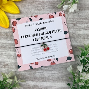 May include: A pink card with a cherry pattern and the text "Make A Wish Bracelet". The card features a black bracelet with a cherry charm. The text reads "Jasmine, I Love You Cherry Much! Love Rose x".