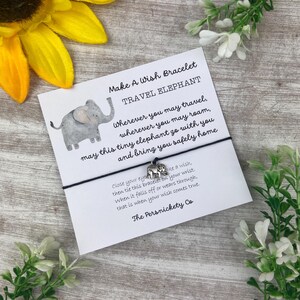 May include: A black string bracelet with a silver elephant charm. The card attached to the bracelet reads "Make A Wish Bracelet Travel Elephant" and includes a message about making a wish and the elephant bringing you safely home. The card is signed "The Persnickety Co."